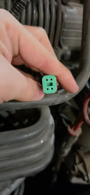 Detalle de un conector verde sostenido frente al sistema de cables de un vehículo